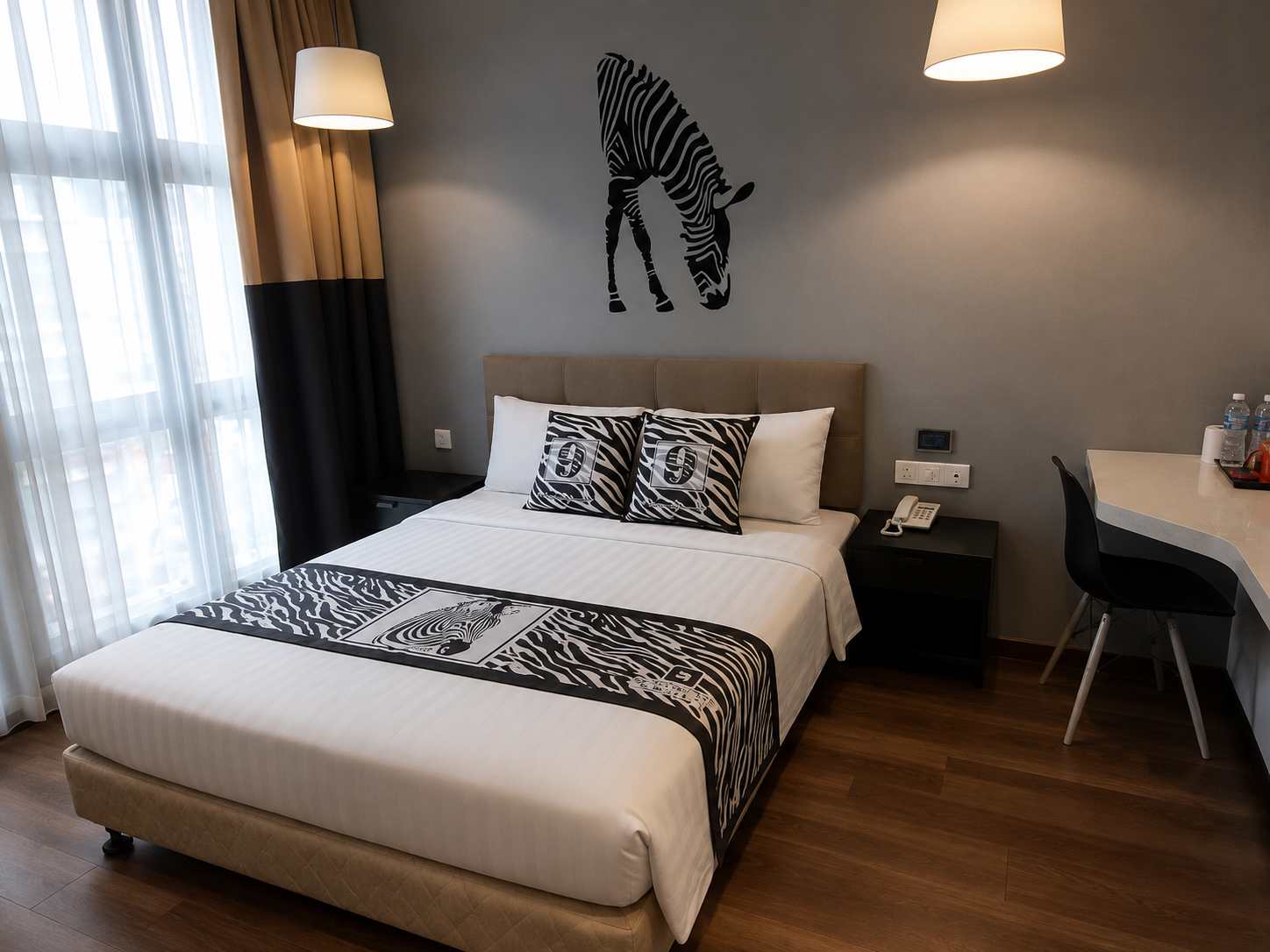 Wide view of a guest room with a large bed, desk and window